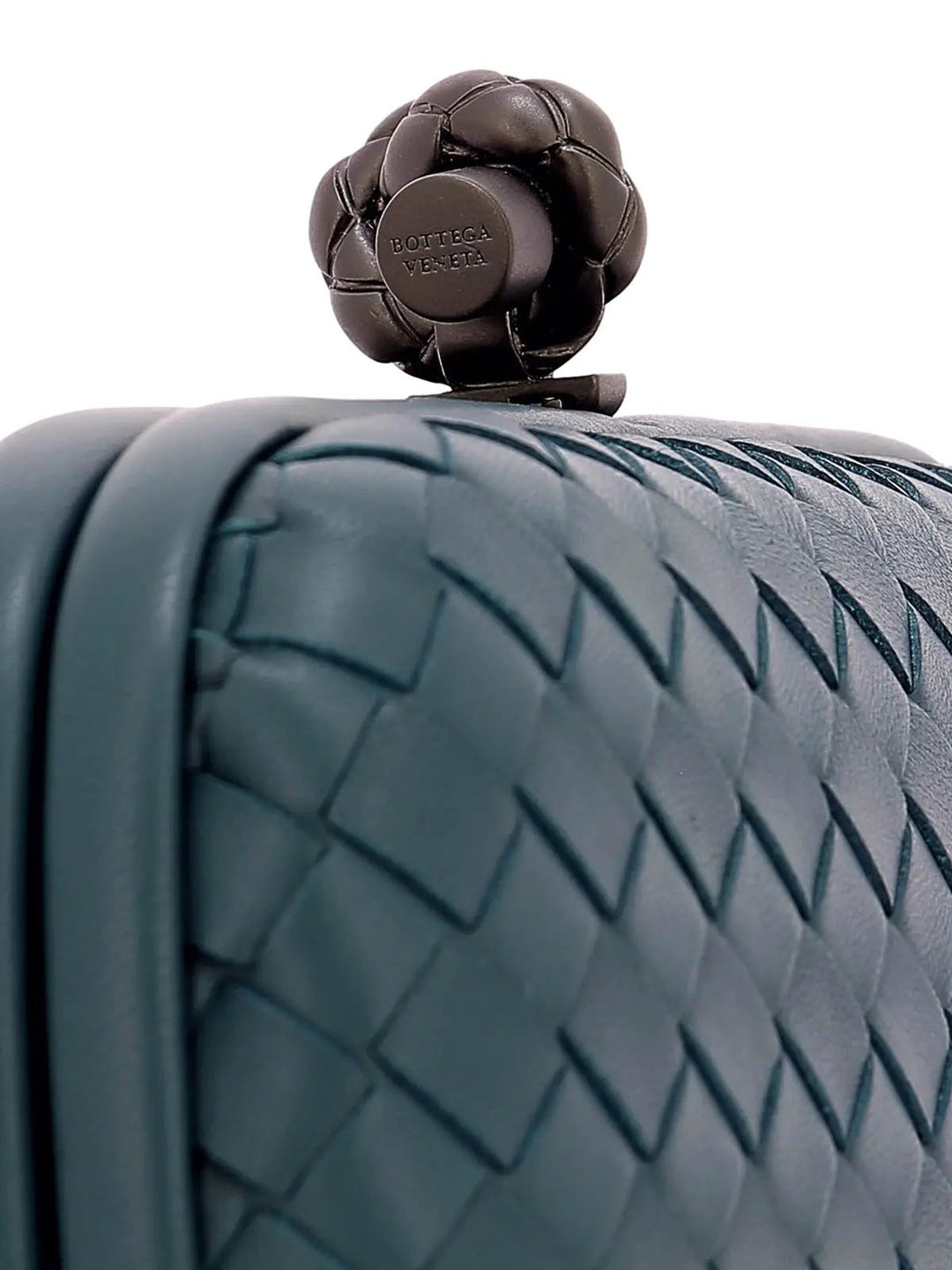 Close-up of a woven leather bag with a dark metallic flower-shaped clasp featuring the embossed brand name Bottega Veneta.