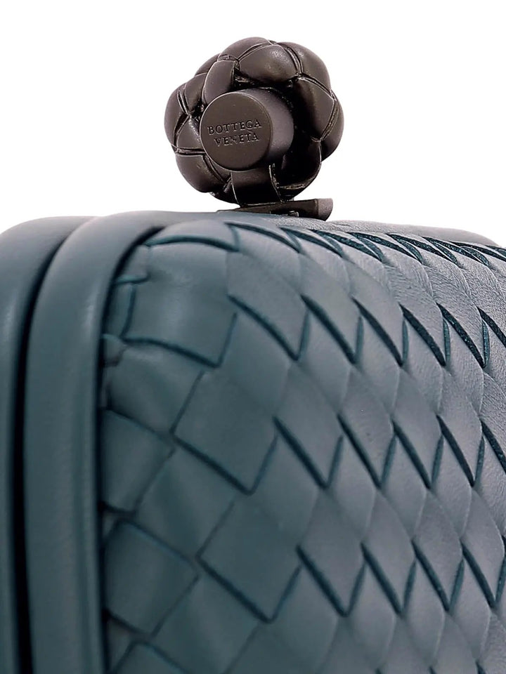 Close-up of a woven leather bag with a dark metallic flower-shaped clasp featuring the embossed brand name Bottega Veneta.