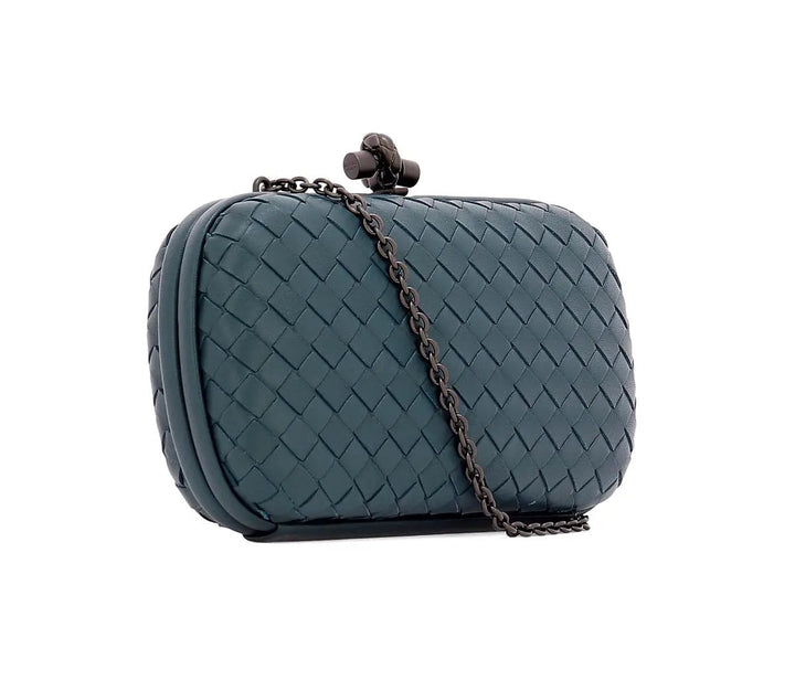 A woven leather clutch bag in a muted teal blue-green color, featuring a dark metal chain strap and a decorative clasp closure, set against a plain white background.