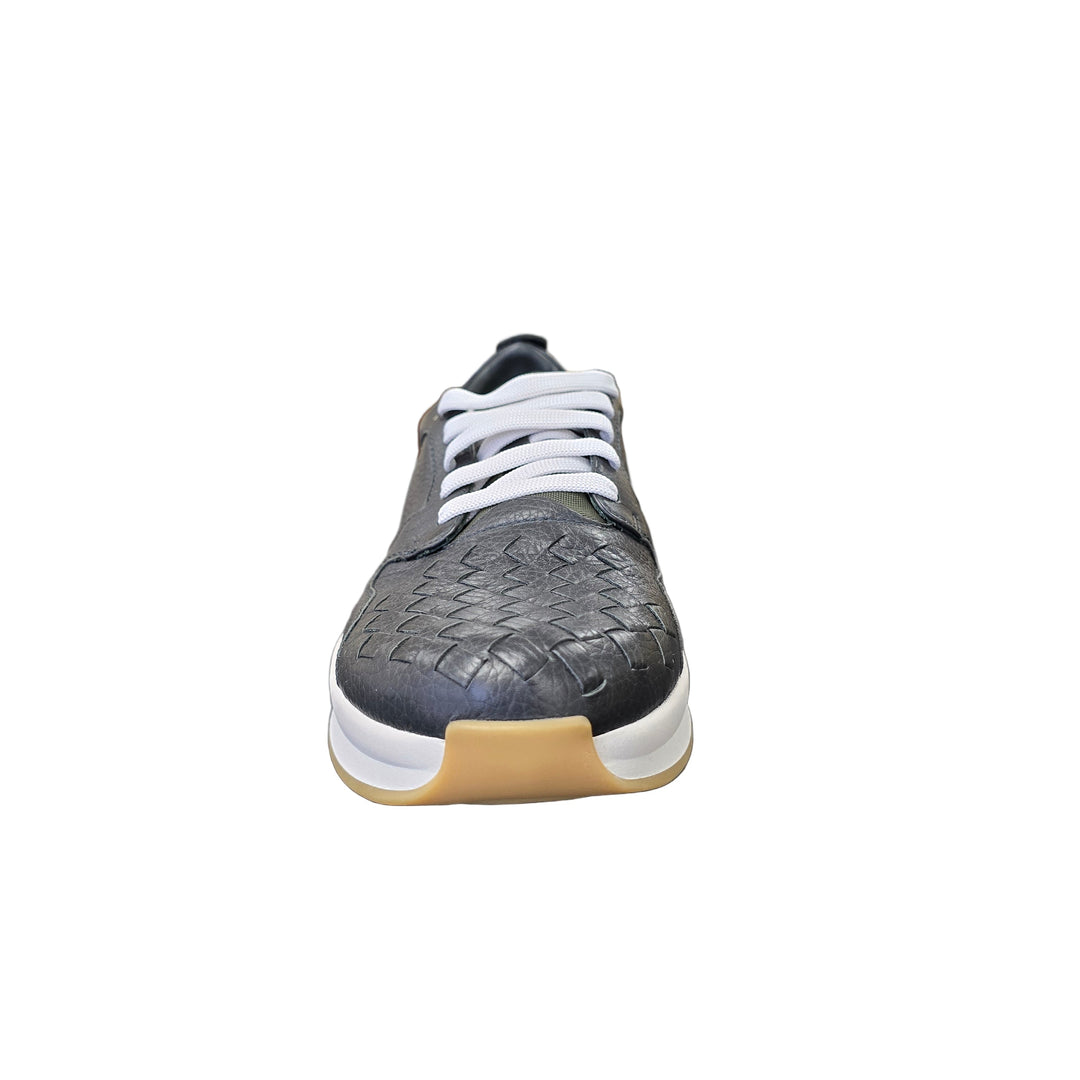 Black and white sneaker with a textured sole on a gray surface, with a blurred indoor background.
